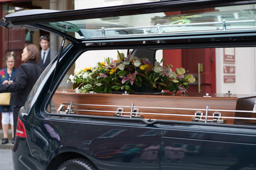 Coffin with floral arrangement inside a funeral hearse outside a service venue in Auckland, provided by Lagoon View Funeral Services.