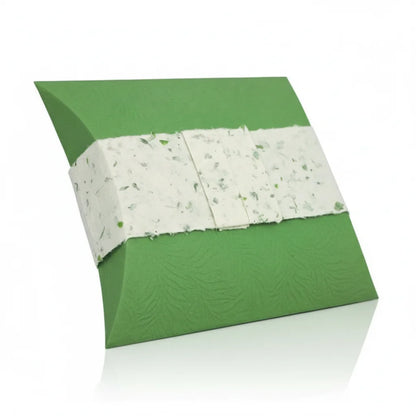 A three-quarter view product shot of an eco-friendly green urn with a textured surface, wrapped with a white, plant-infused band. The urn rests on a reflective white studio background with soft, even lighting, highlighting its sustainable design and natural elements